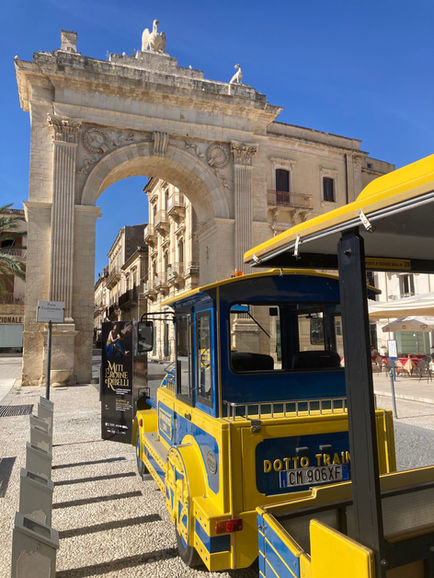 Treno turistico giallo e blu accanto a un grande arco in pietra