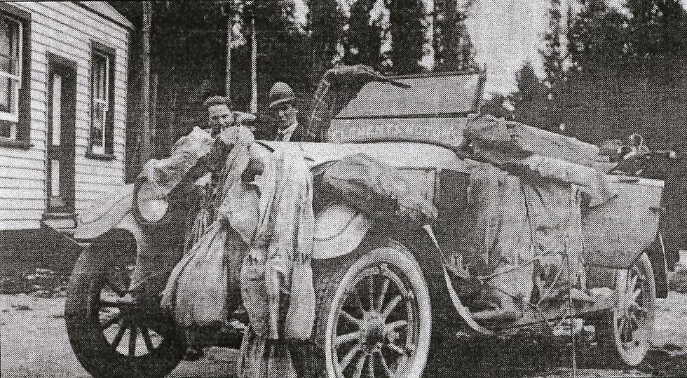 An old style car with bags of mail filling the inside and attached all around the outside