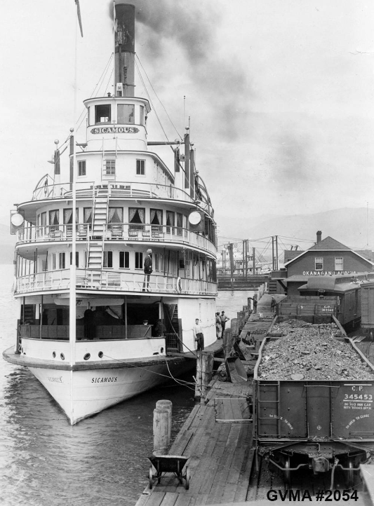 two coal cars, SS Sicamous, at dock with barge and building in background