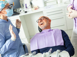 older man sitting in a dental chair talking to dentists around him