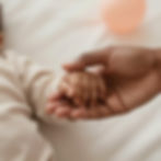 An adult's hand holding a baby's hand for maternal support services.