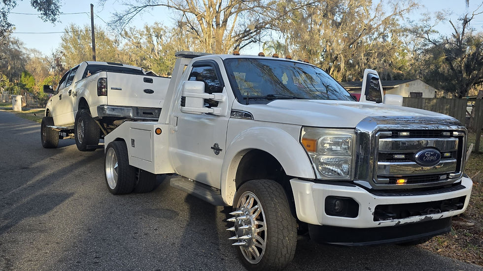 White Ford tow truck hauling a white pickup, junk cars for cash.