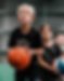 A young boy aged around 7 with blonde hair holds a basketball and looks like he is concentrating on the basketball hoop