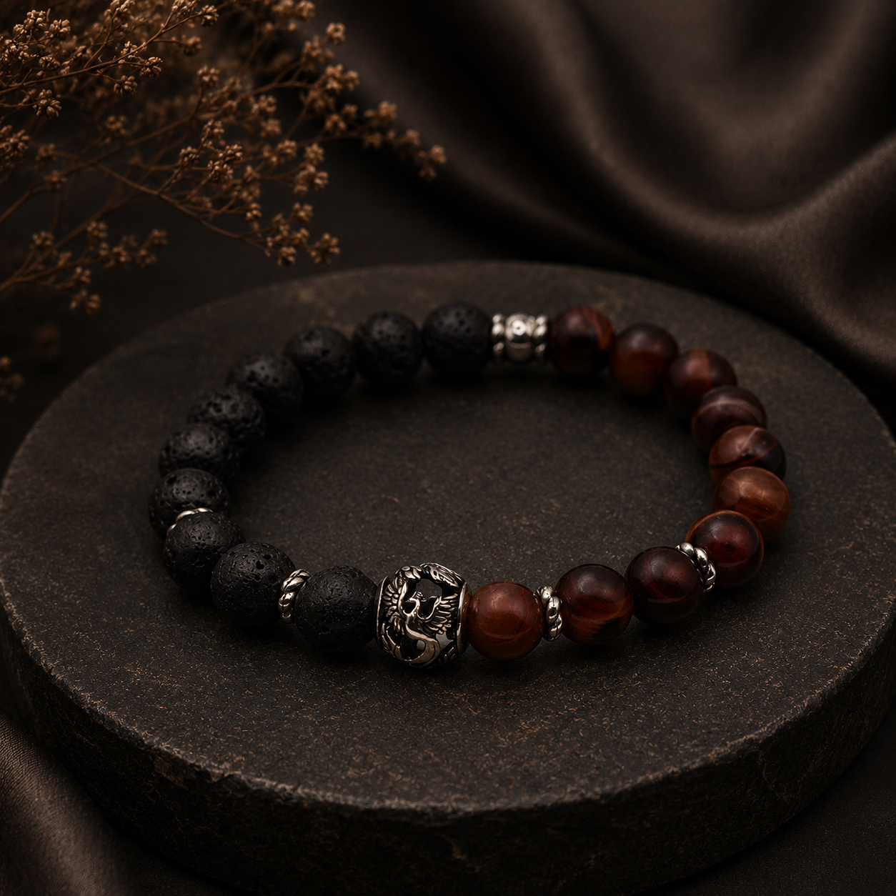 Herrenarmband aus Lavastein und rotem Achat mit Phönix-Motiv auf dunklem Natursteinpodest in edlem Ambiente.