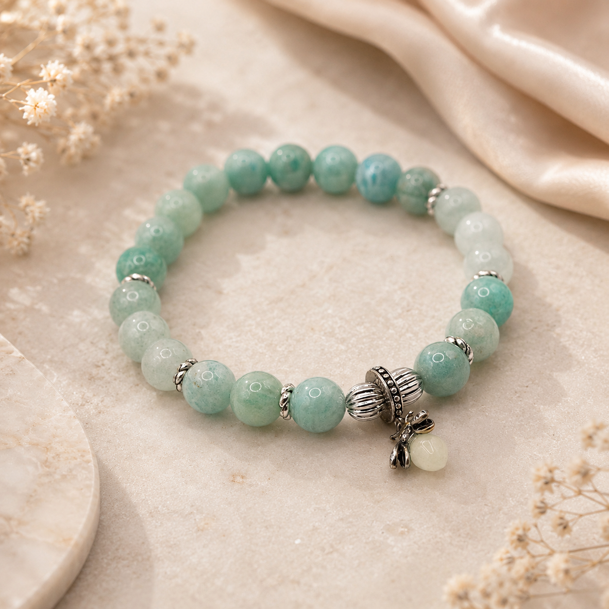 Armband aus Aquamarin und burmesischer Jade mit Glühwürmchen-Anhänger auf hellem Naturstein.