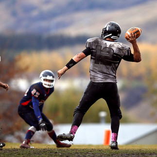 Three suited up football players in a field, with one player ready to throw the ball.