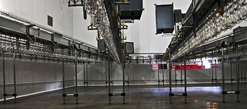 Interior de fábrica industrial oscura con cadenas aéreas; ambiente de producción. solferinoweb