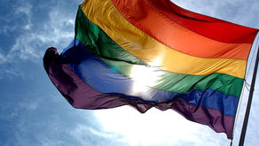 Foto de uma bandeira LGBT com céu azul de fundo