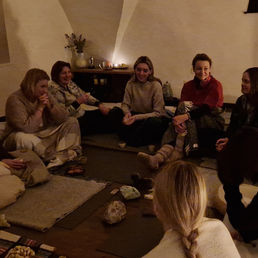 Moterų ratas jaukioje erdvėje po garso terapijos – dalyvės sėdi ratu, šnekučiuojasi ir dalijasi patirtimis Joga Nidra Kristaluose renginyje.