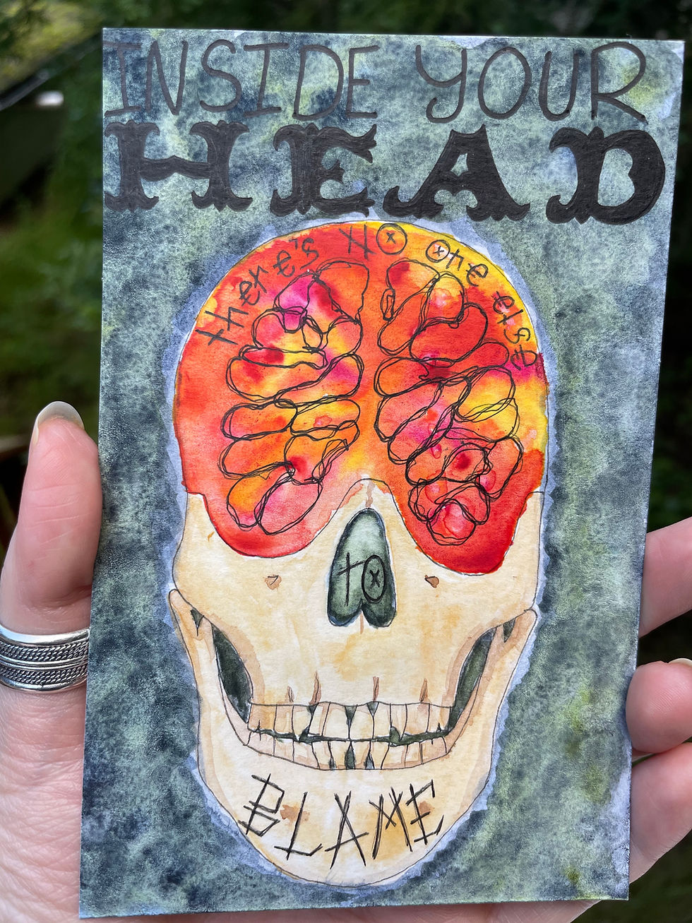 A painting of a skull with the brain cavity in bright warm colors reading "Inside your head there's no one else to blame"
