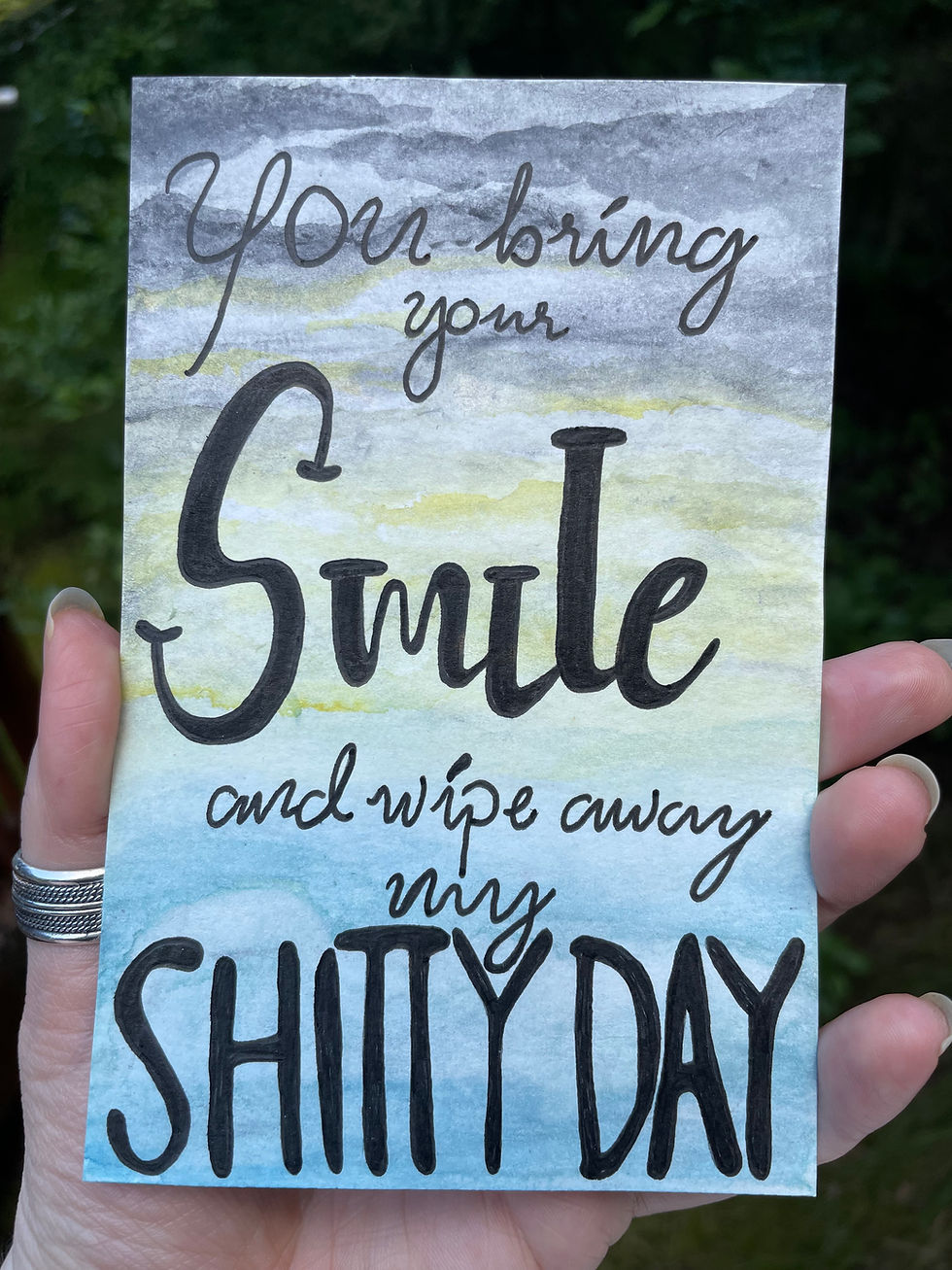 A painting of a cloudy sky breaking into a sunny blue sky with the words "you bring your smile and wipe away my shitty day"
