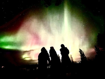Três viajantes olhando para a Aurora Boreal no céu.