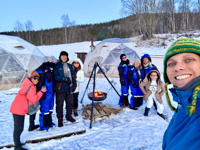 Grupo de viajantes ao redor de uma fogueira acesa, em frente a iglus para hospedagem e observação da Aurora Boreal.