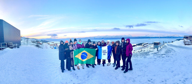 Grupo de cerca de 15 viajantes posa em meio à neve, segurando uma bandeira do Brasil e outra onde lê-se "Somos Domundo".