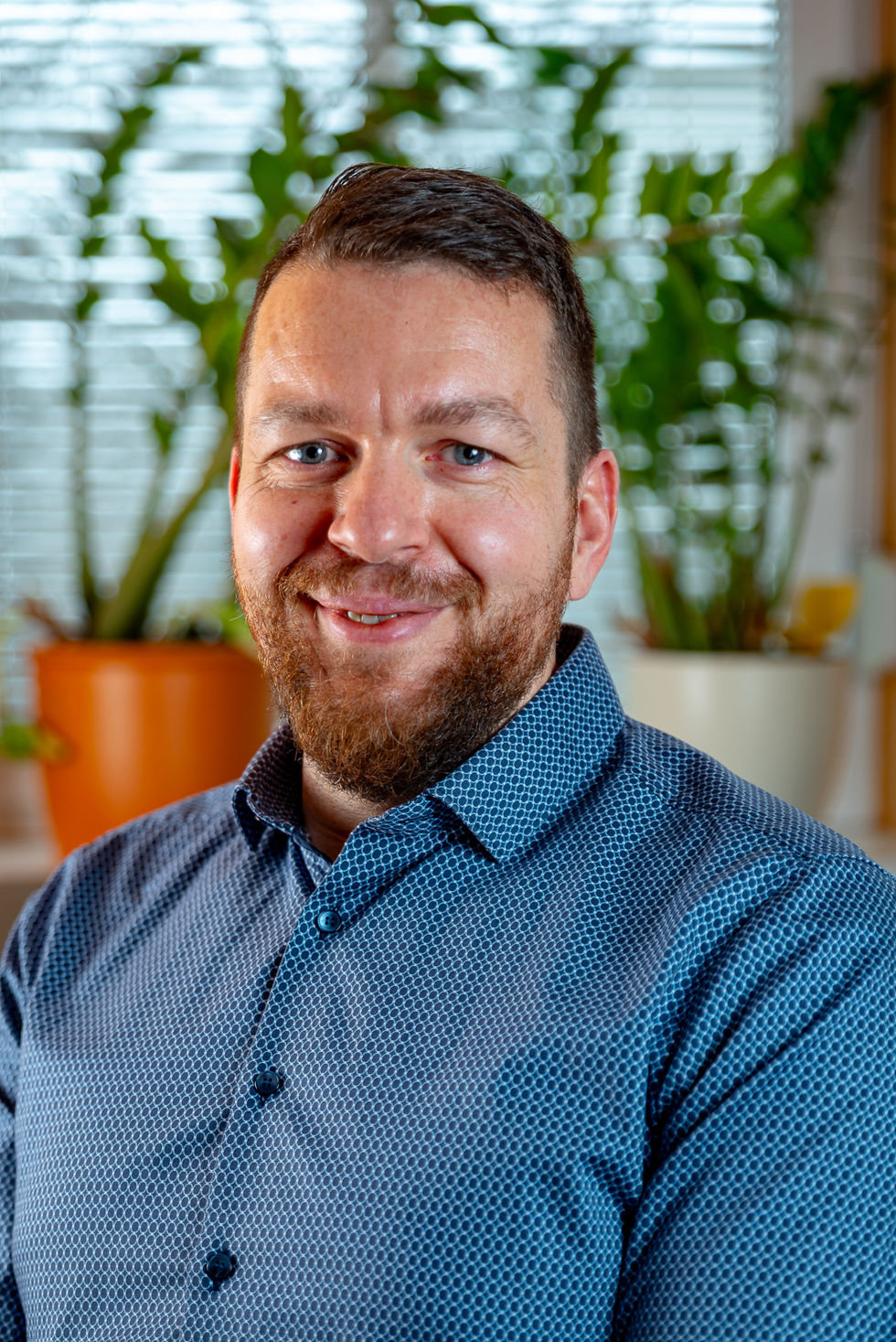 Professionelles Business-Portrait eines Mannes mit blauem Hemd und Bart vor unscharfem Hintergrund.