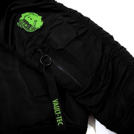 Black tactical bomber with a strap pouch in the back and various zippered compartments on the sleeves and front. Fallout text logo in bright green over the left chest on the front, Vault Boy VATS from Fallout is printed on the back in bright green, embroidered Vault Boy head patch in bright green on the left sleeve, and embroidered Vault-Tec patch on the right sleeve