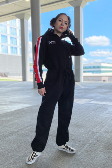 An N7 from Mass Effect themed onesie or kigurumi, which is all black and has the signature N7 red/white stripe on the right arm, N7 embroidery over the right chest, and custom N7 printed fabric on the hoodie