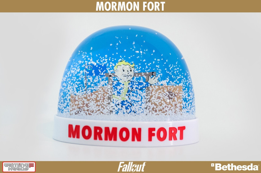 A real life collectible plastic snow globe based on Old Mormon Fort as seen in Fallout: New Vegas. Vault Boy waving at the entrance to the Fort. The snow globe has a clear plastic dome, with a white base that says MORMON FORT capitalized red text on the front