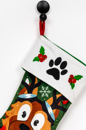 Holiday themed stocking and ornament set featuring Dogmeat from Fallout 4. The stocking shows a portrait of Dogmeat sticking his tongue out while wearing reindeer horns, surrounded by holly, snowflakes, and festive lights. He's also wearing a Vault 111 bandana that overlaps the stocking. The matching ornament features Dogmeat wearing his signature goggles, with a grey ribbon for hanging
