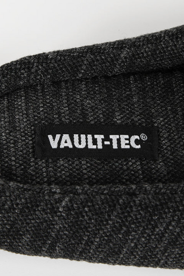 A pair of dark heathered grey house slippers with yellow embroidered Vault-Tec logos from Fallout on the outside of the slippers, and a repeating Vault-Tec logo pattern on the soles