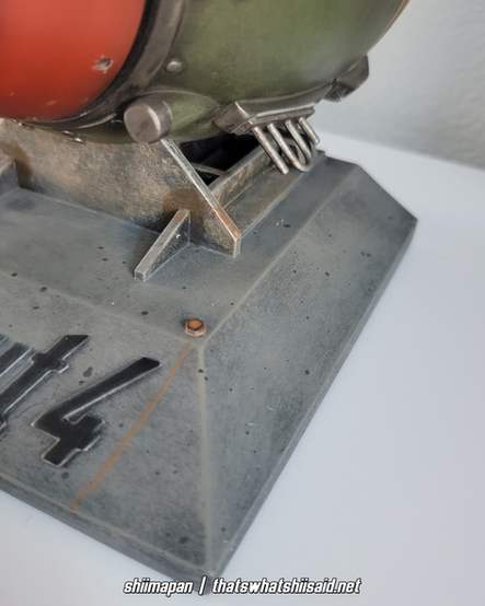 A set of bookends modeled after a mini nuke from Fallout 4, also pictured with a large silver enamel pin of Liberty Prime tossing a mini nuke