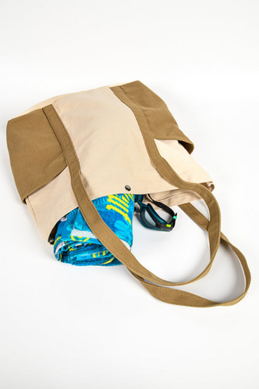 A Vault Boy from Fallout themed beach towel, featuring a repeating Vault Boy perks pattern in the foreground and teal tropical leaves on a blue in the background