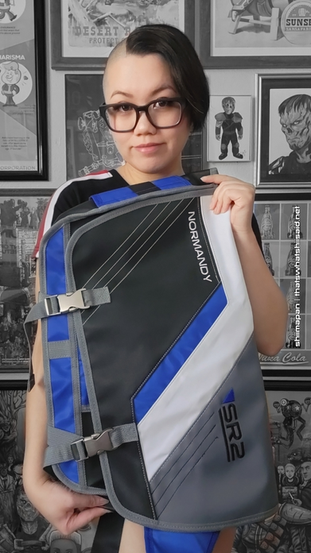 Selfie of a girl wearing a girl with short hair and glasses, wearing a N7 from Mass Effect shirt paired with light denim shorts. She's also carrying a SR2 Normandy Alliance from Mass Effect themed cross shoulder messenger bag