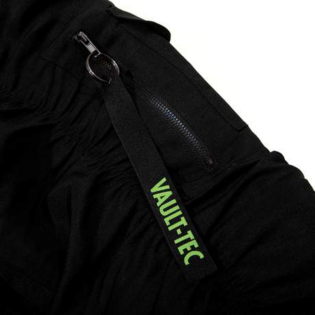 Black tactical bomber with a strap pouch in the back and various zippered compartments on the sleeves and front. Fallout text logo in bright green over the left chest on the front, Vault Boy VATS from Fallout is printed on the back in bright green, embroidered Vault Boy head patch in bright green on the left sleeve, and embroidered Vault-Tec patch on the right sleeve