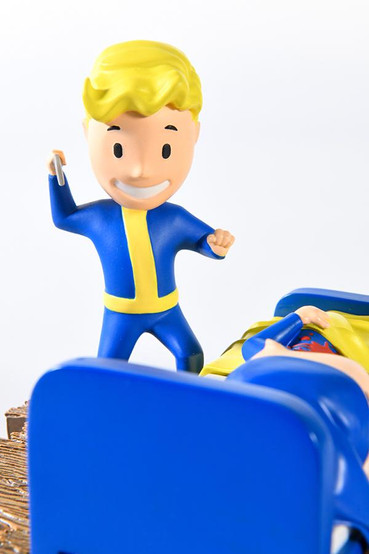 Vault Boy from Fallout mini statues based on various perks from the series, this one is a special variant in technicolor. One Vault Boy is laying in bed with a sleeping cap with a large red stab wound in the middle of his chest, while another Vault Boy is smiling leaning over him with a knife in his right hand