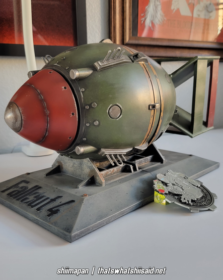 A set of bookends modeled after a mini nuke from Fallout 4, also pictured with a large silver enamel pin of Liberty Prime tossing a mini nuke