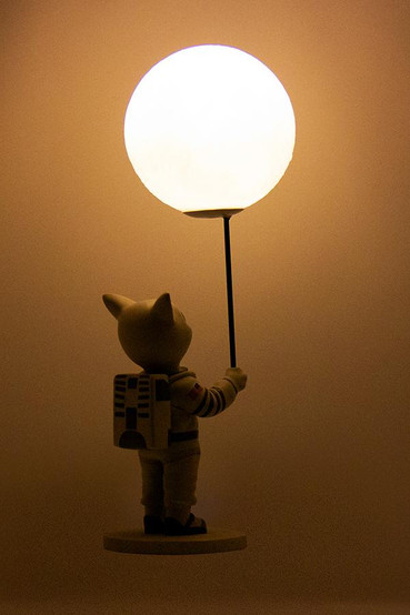 Mr. Pebbles (a white cat with blue eyes wearing a white space suit) from Fallout 76 desk lamp with the light turned on, back profile
