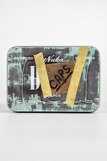 Nuka-Cola Dark (Nuka Dark) from Fallout themed metal tin that comes with 20 matching bottle caps. The front of the tin has a Nuka-Cola Dark label that has the look of a handwritten note that says 'CAPS' taped on front, all with black and grey colorway. The loose bottle caps have the Nuka-Cola Dark logo in a script font on the front of the cap, with the inside of the bottle cap a silver color