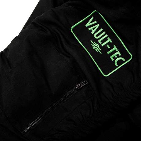 Black tactical bomber with a strap pouch in the back and various zippered compartments on the sleeves and front. Fallout text logo in bright green over the left chest on the front, Vault Boy VATS from Fallout is printed on the back in bright green, embroidered Vault Boy head patch in bright green on the left sleeve, and embroidered Vault-Tec patch on the right sleeve