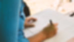 Close-up of a pencil correcting a spelling error on paper. "Diedbure" is underlined in red. Spiral notebook edges visible.