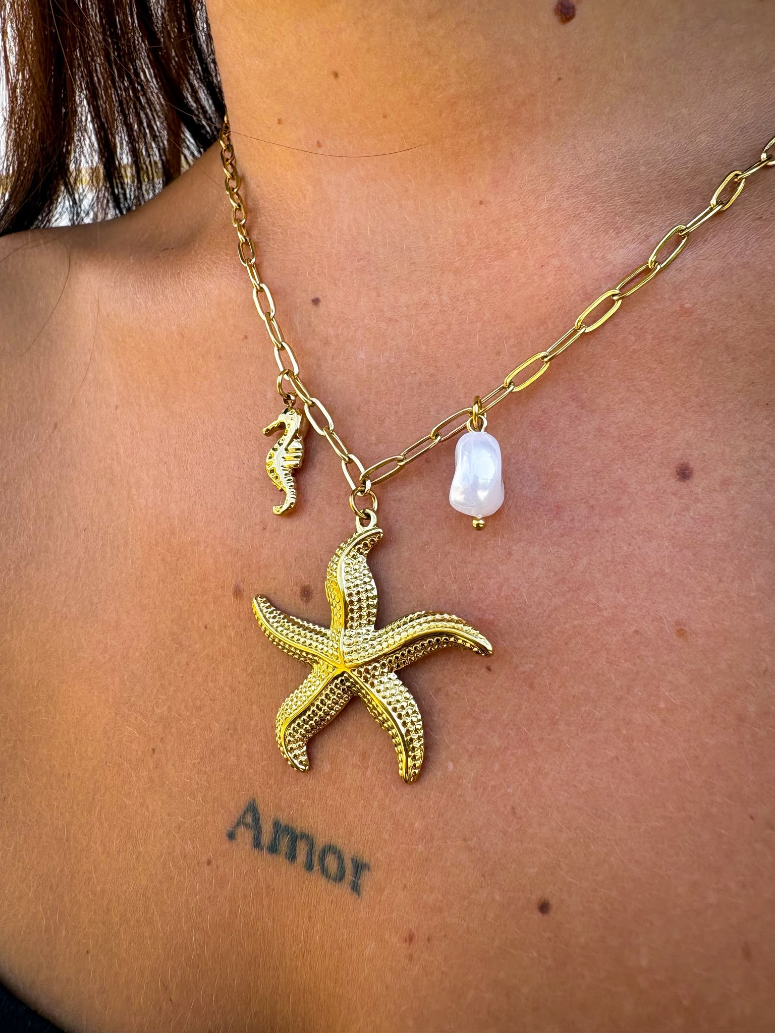 Un collier doré esprit bord de mer, composé de charms marins : étoile de mer, hippocampe et perle blanche. Une pièce solaire
