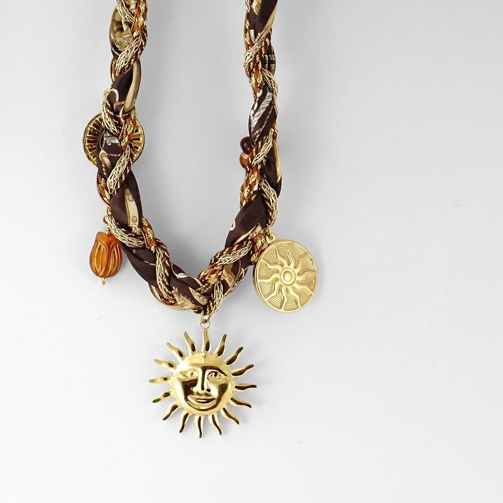 Miniature : Un collier original et solaire mêlant chaîne dorée, foulard en tissu et pendentifs dorés. Le grand soleil central illumine la