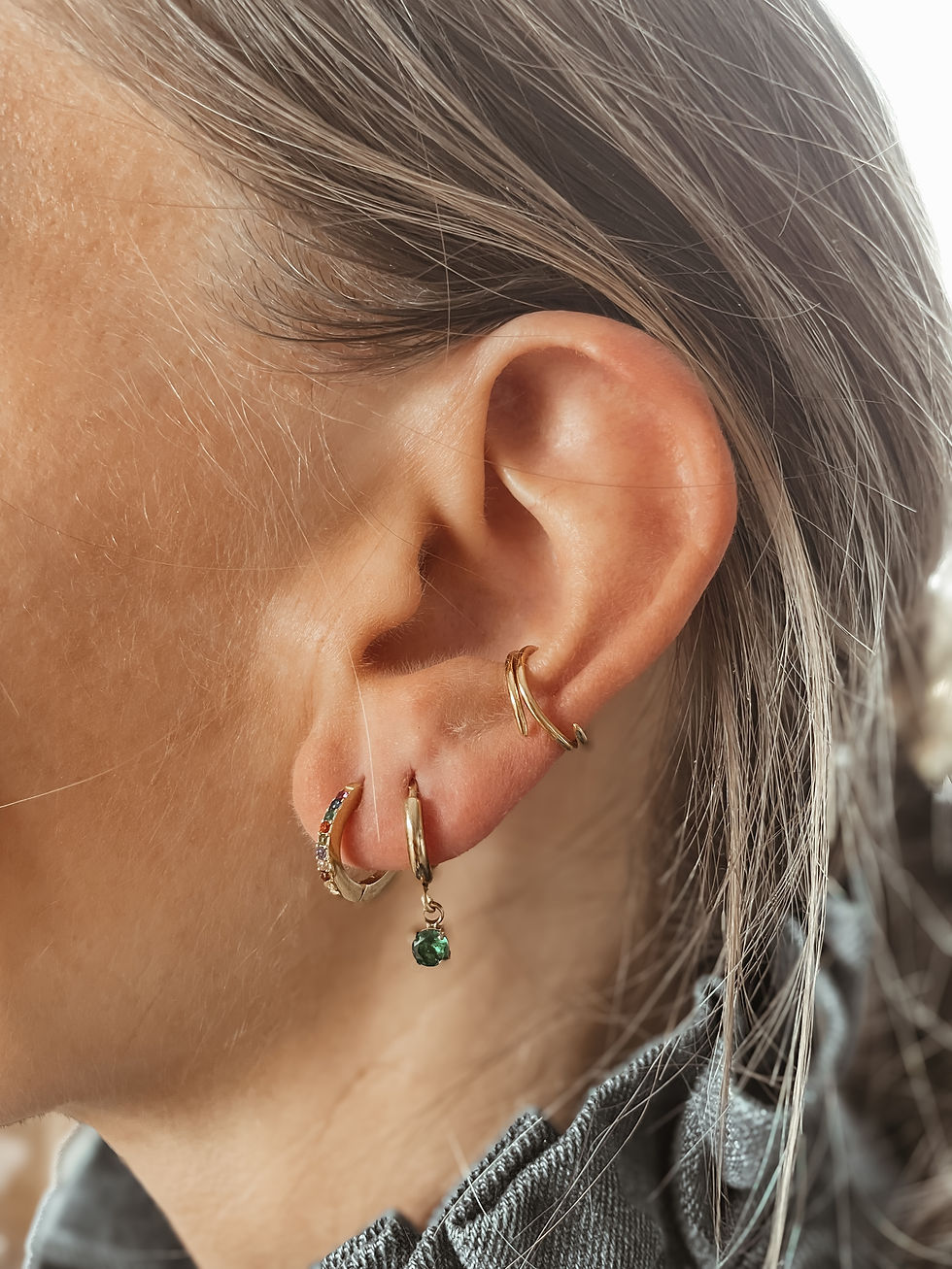 Créoles fines agrémentées d’un petit solitaire vert suspendu. Délicates mais lumineuses, elles twistent un look simple en un