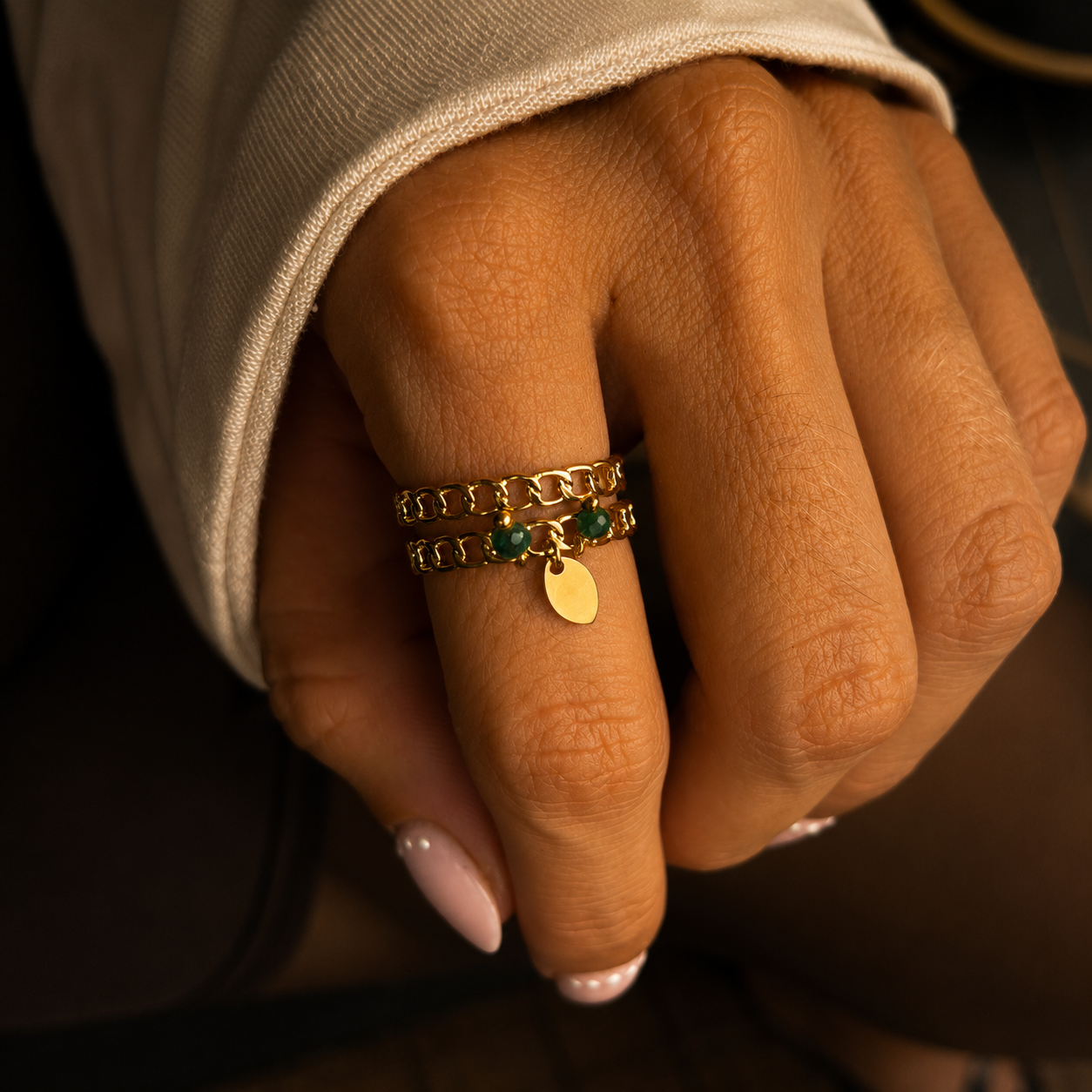 bague Oyana mêle plusieurs rangs façon chaîne à de petites perles vertes et un pendentif doré