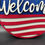 Thumbnail: Round sign designed as an American flag with Welcome in white script over a blue background, stars, and red and white stripes