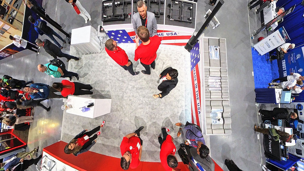 Overhead 360-degree view of the K2 Systems booth at InterSolar North America 2025. Several team members in red shirts are engaged in discussions with attendees, while the booth displays solar mounting solutions with ‘Made in the USA’ branding. Surrounding booths and expo attendees are visible in the background, showcasing a busy trade show environment.