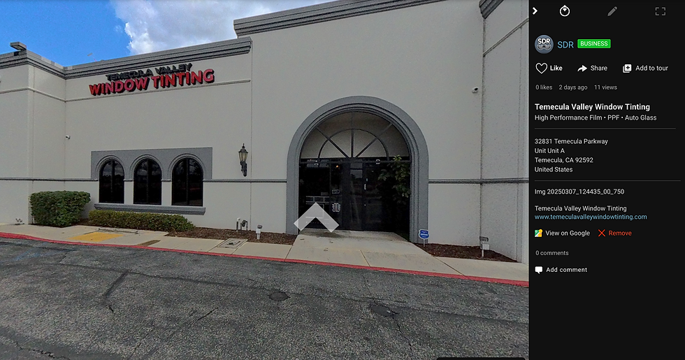 Exterior of Temecula Valley Window Tinting building located at 32831 Temecula Parkway, Unit A, Temecula, CA 92592. The building has a light gray facade with darker gray accents, arched windows, and a large glass entrance door framed by a decorative arch. The business name 'TEMECULA VALLEY WINDOW TINTING' is displayed in bold red and black lettering on the upper left corner of the building. A lantern-style light fixture is mounted on the wall near the entrance, and there are neatly trimmed bushes along the front. The parking area has a red curb and wheelchair-accessible sidewalk ramp.