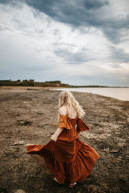 Little girl with blonde hair and rust long dress, twirling on the beach