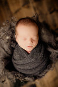 Newborn boy sleeping peacefully wrapped in charcoal gray wrap in a wooden box