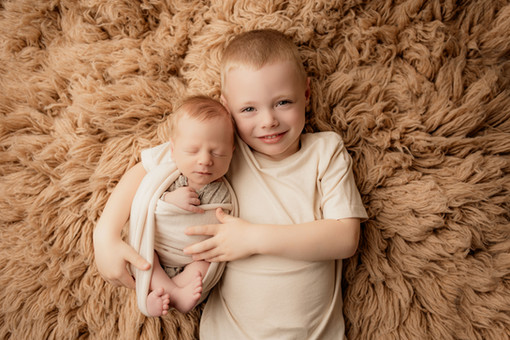 Big brother gently holding newborn baby and smiling softly