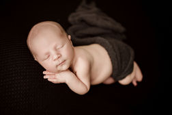 Newborn boy snuggled soundly on a black blanket with hands up by cheek