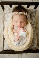 Newborn girl in pale yellow wrap, with dark hair, sleeping peacefully