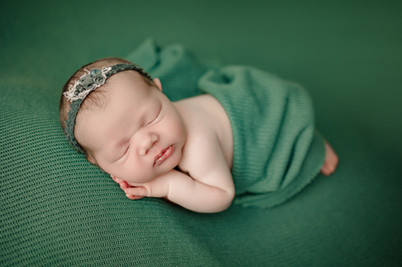 A newborn baby girl sleeping with her hands pulled up to her face