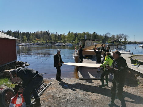 Wolfbuilders team lastar byggmaterial på en arbetsbåt vid en brygga i Stockholms skärgård, omgiven av naturskön miljö och klarblå himmel.
