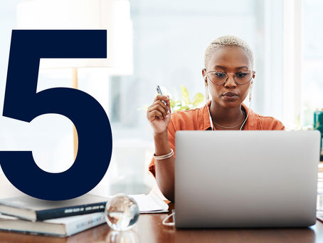 Woman working on a laptop in a bright room, wearing glasses and earbuds. Large blue "5" and books on desk. Focused and professional mood.