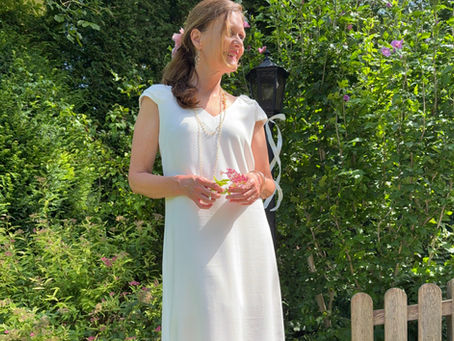 Frau im weissen Kleid vor grünen Büschen und Laterne mit weißem Band